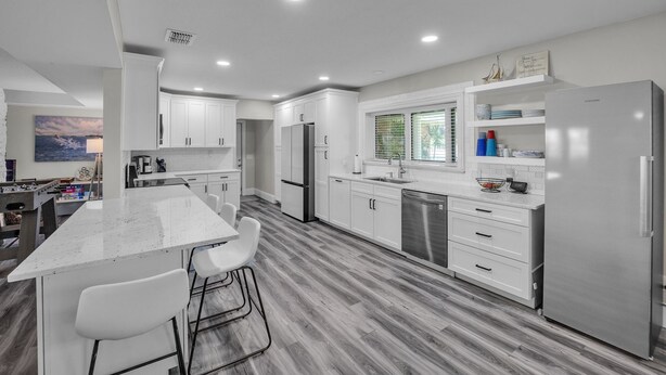 A modern kitchen with white cabinetry, a stainless steel refrigerator, and a dining area with a white table and chairs. - Beautiful Lake View Retreat Drivable To Theme Parks 3 Bedroom Home (Haines City)