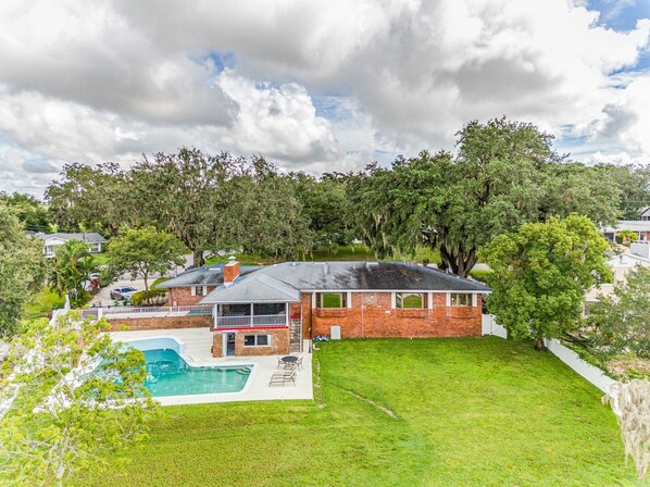 A two-story house with a brick exterior, a swimming pool, and a well-maintained lawn. - Beautiful Lake View Retreat Drivable To Theme Parks 3 Bedroom Home (Haines City)