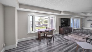 A spacious living area with a large window, a wooden coffee table, a sofa, and a TV. - Beautiful Lake View Retreat Drivable To Theme Parks 3 Bedroom Home (Haines City)