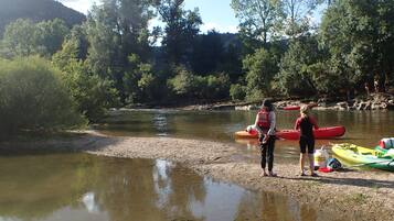 Orilla de río con kayaks y una persona con chaleco salvavidas.
