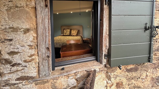 Una habitación rústica de piedra con una puerta de madera que da a una cama con ropa de cama floral.