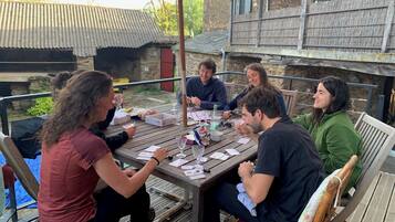 Un groupe de personnes est assis autour d’une table en bois à l’extérieur, avec un bâtiment en pierre en arrière-plan.