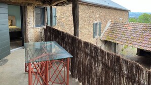 Un edificio rústico de piedra con techo de paja y una mesa de vidrio con patas rojas.
