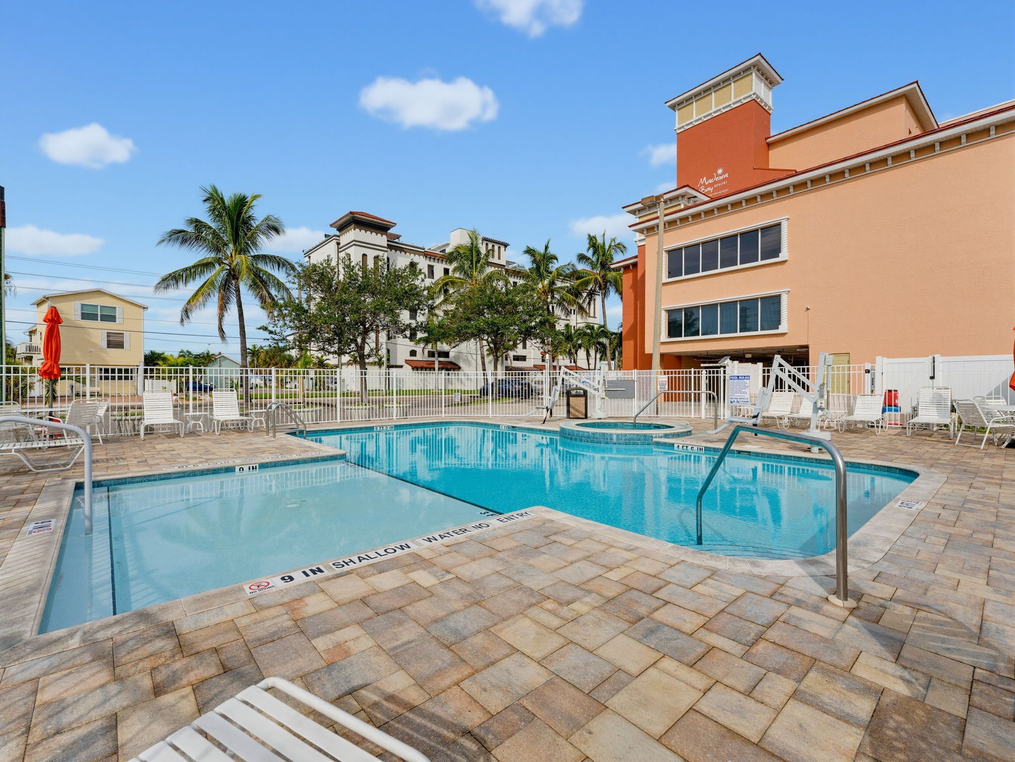 A pool area with two swimming pools, palm trees, and a building with a sign that reads 'Malaqua Bay Resort'.