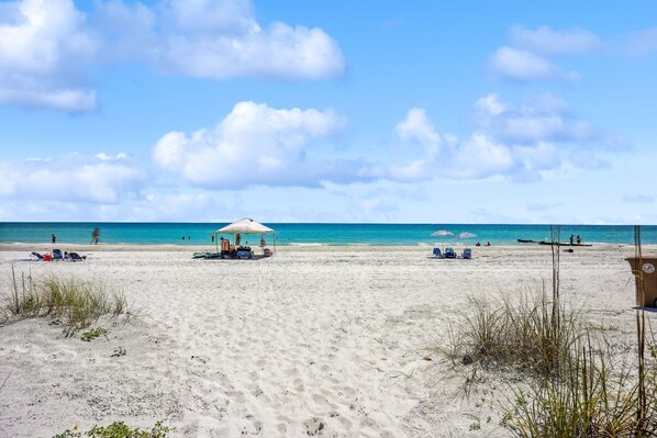 A beach with clear skies, a few umbrellas, and people in the distance.