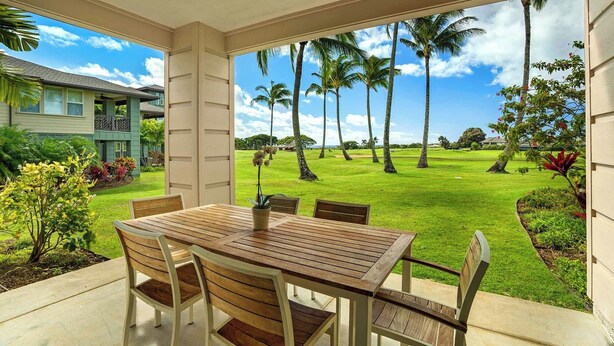 Une terrasse couverte, avec une table et des chaises en bois, donnant sur une pelouse bien entretenue, agrémentée de palmiers et avec un terrain de golf en arrière-plan.