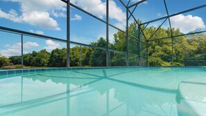 An indoor swimming pool with clear blue water, surrounded by a metal fence and trees in the background. - Spacious 4-bed lakeside pool villa near Disney (Kissimmee)