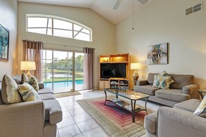 A spacious living room with a large TV, comfortable seating, and a view of a pool. - Spacious 4-bed lakeside pool villa near Disney (Kissimmee)
