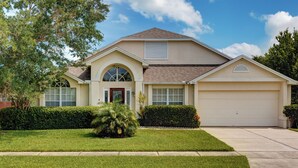 A single-story house with a garage, a front entrance with a door, and a small front yard with grass and a bush. - Spacious 4-bed lakeside pool villa near Disney (Kissimmee)
