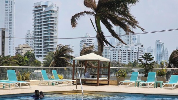 A swimming pool with lounge chairs and a gazebo, surrounded by palm trees and high-rise buildings in the background. - PARCEROS GROUP - 2 BEDROOM VACATION APARTMENT, 10TH FLOOR, CARTAGENA, SPAIN (Cartagena de Indias)