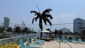 A rooftop terrace with lounge chairs, a palm tree, and a view of a city skyline. - PARCEROS GROUP - 2 BEDROOM VACATION APARTMENT, 10TH FLOOR, CARTAGENA, SPAIN (Cartagena de Indias)