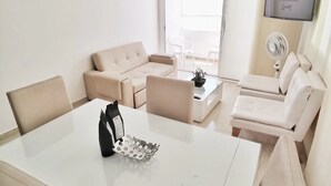 A modern living room with a white table, beige sofas, and a TV mounted on the wall. - PARCEROS GROUP - 2 BEDROOM VACATION APARTMENT, 10TH FLOOR, CARTAGENA, SPAIN (Cartagena de Indias)