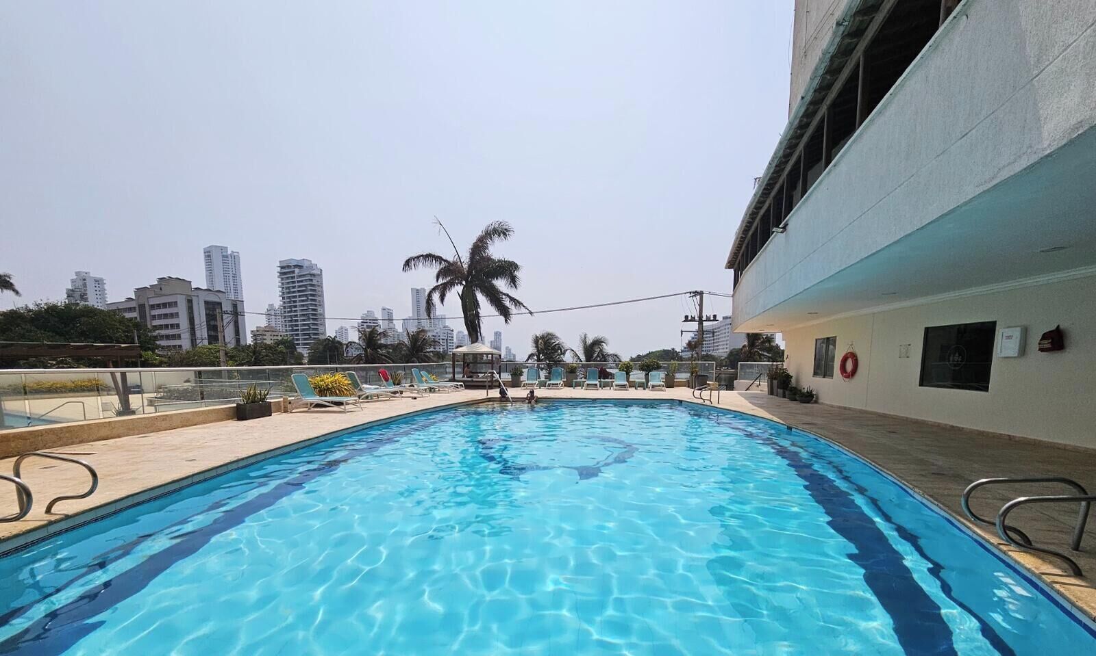 A swimming pool with lounge chairs and a palm tree, surrounded by a cityscape.