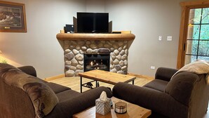 A living room with a stone fireplace, a television, and two couches. - Cozy 2-bedroom cabin steps away from starved rock state park (North Utica)