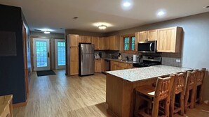A modern kitchen with wooden cabinets, a stainless steel refrigerator, a microwave, and a granite countertop island with wooden chairs. - Cozy 2-bedroom cabin steps away from starved rock state park (North Utica)