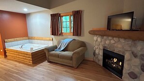 A spacious living room with a large wooden floor, a stone fireplace, a sofa, a TV on a wooden shelf, and a window with curtains. - Cozy 2-bedroom cabin steps away from starved rock state park (North Utica)