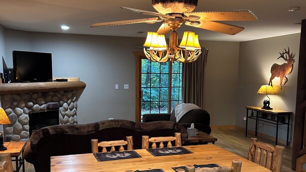 A dining area with a wooden table and chairs, a stone fireplace, and a ceiling fan. - Cozy 2-bedroom cabin steps away from starved rock state park (North Utica)