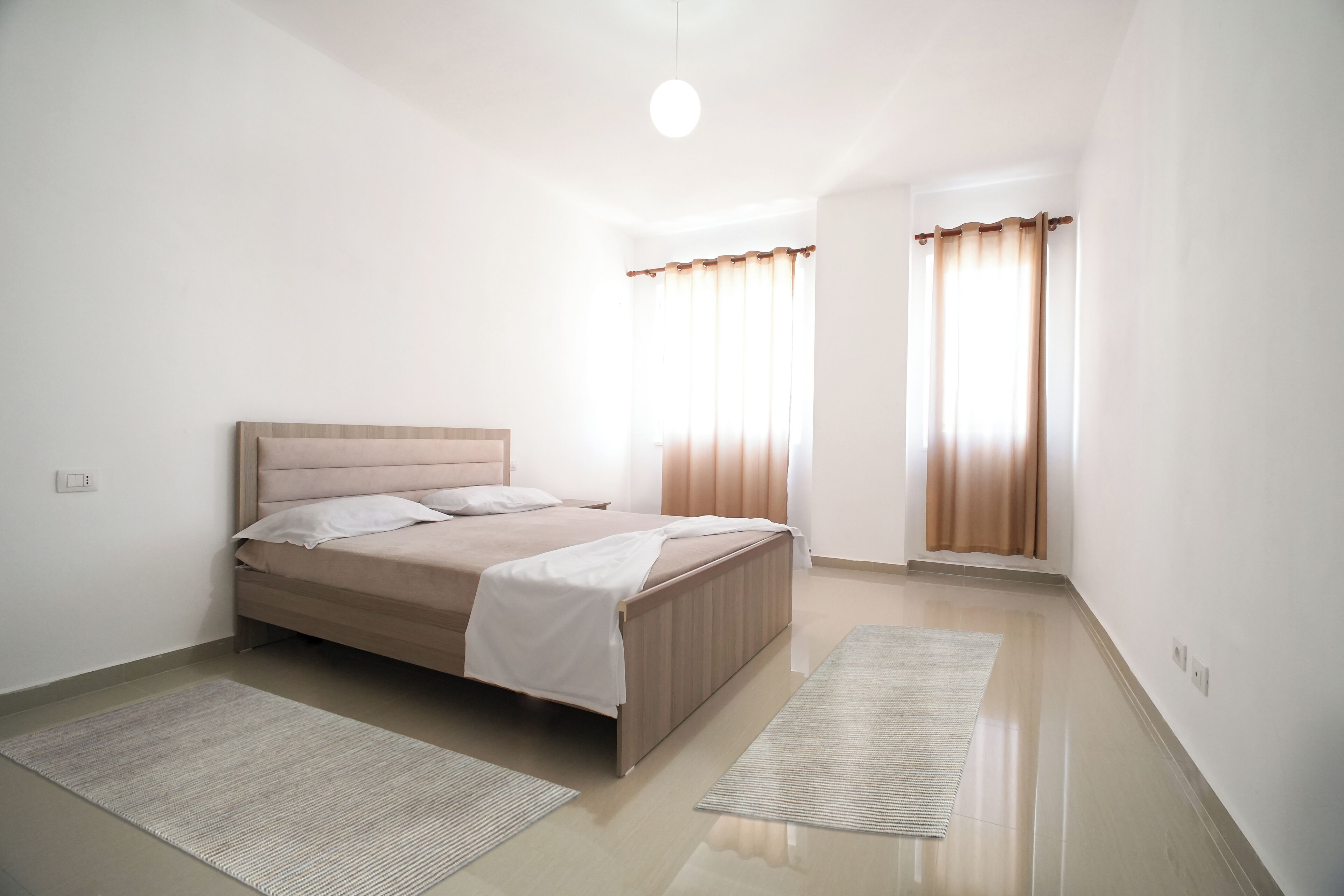 A bedroom with a bed, two rugs, and curtains on the windows.