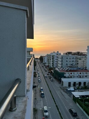 A city street at sunset with buildings and parked cars.