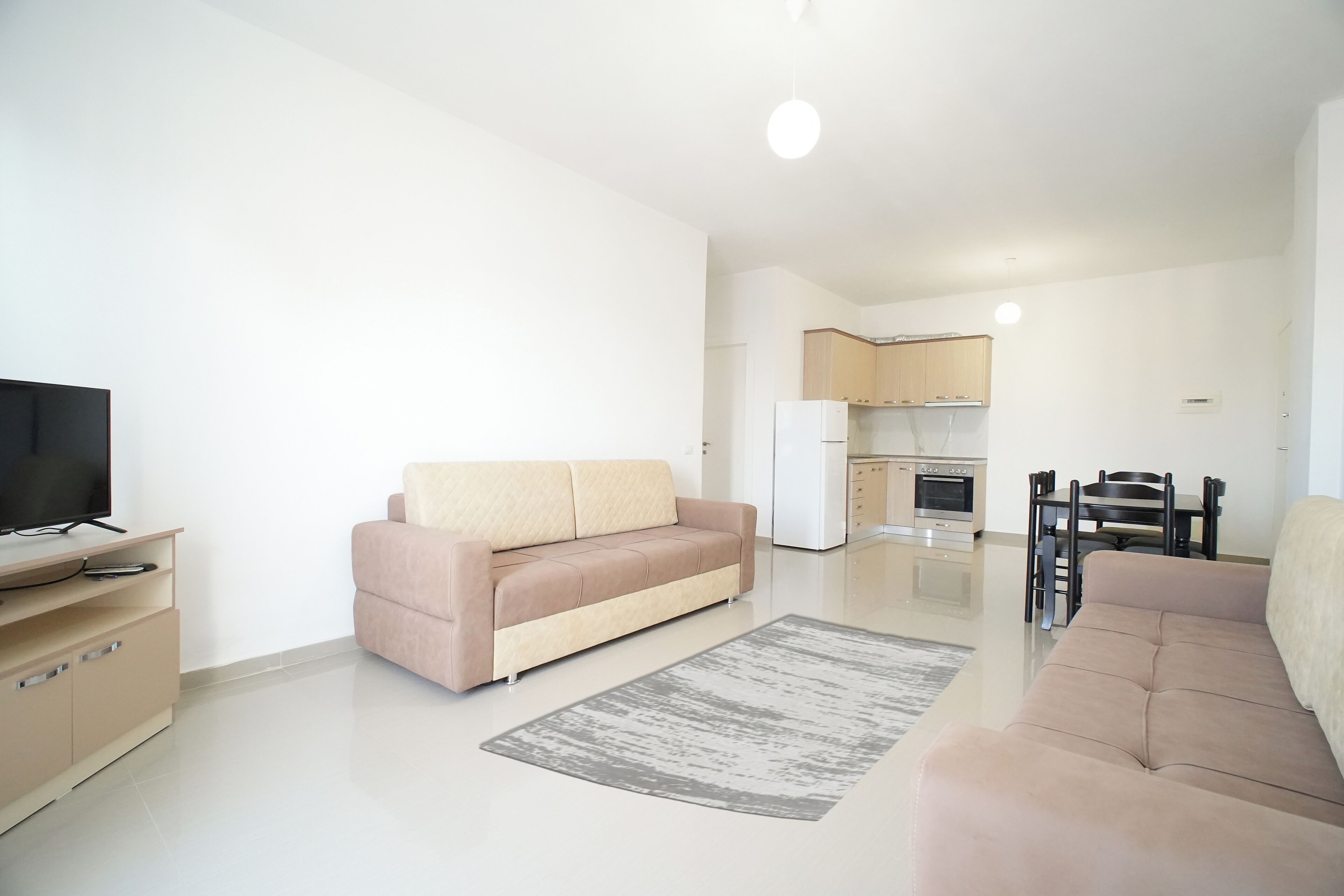 A modern living room with a beige sofa, a TV, and a dining area with a table and chairs.