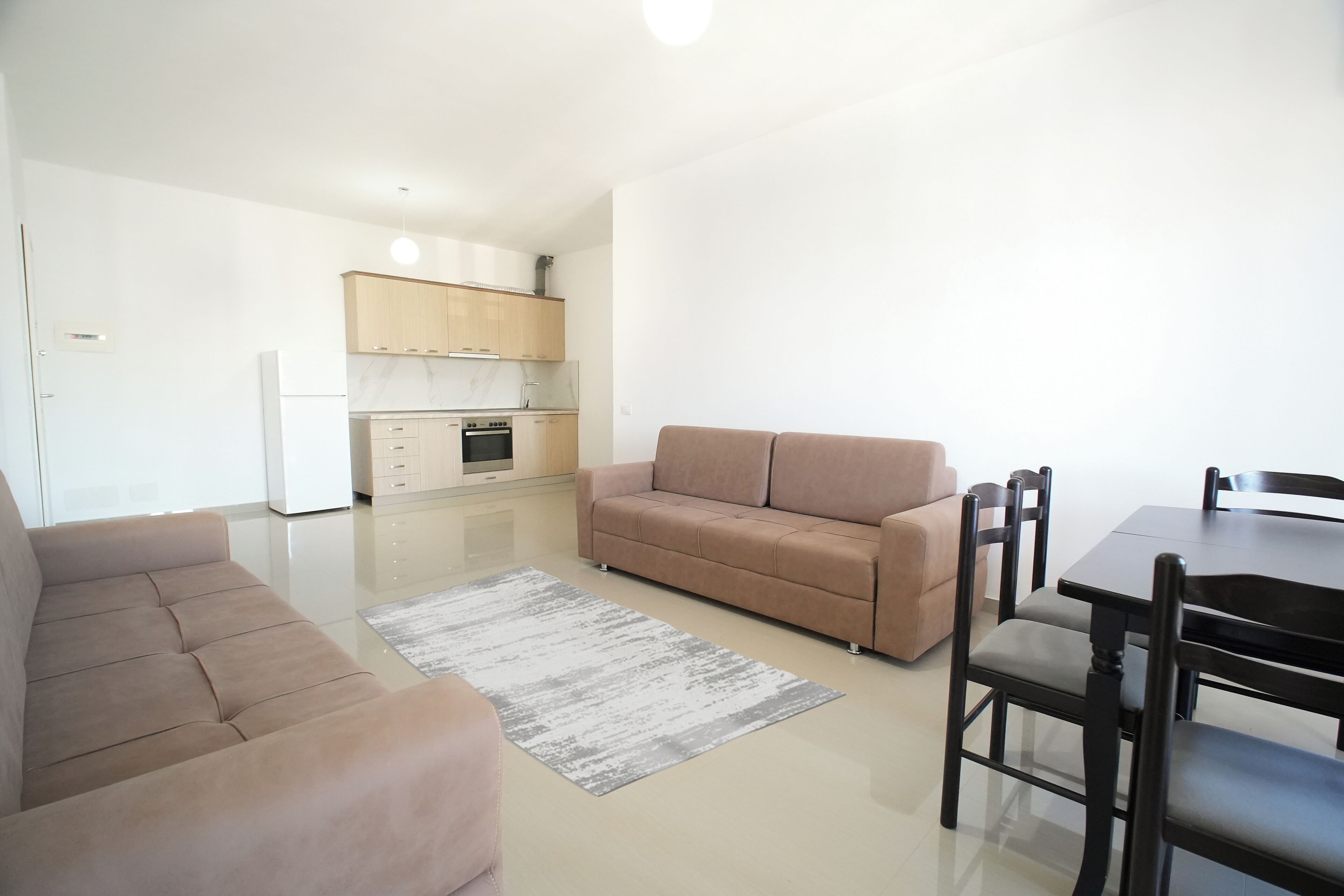 A modern living room with a sofa, a dining table with chairs, and a kitchen in the background.