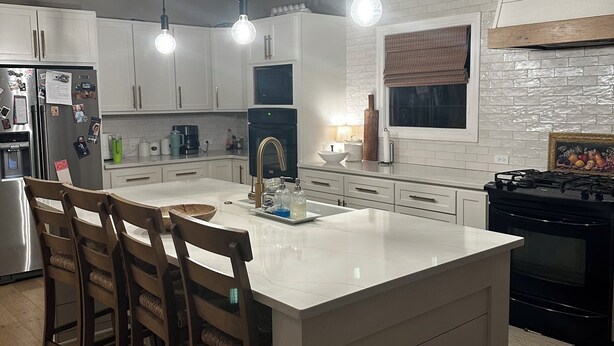 Een moderne keuken met een centraal eiland, witte kasten en hanglampen.