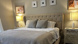 Een slaapkamer met een groot bed, een bankje, twee nachtkastjes met lampen, en een muur met ingelijste foto's.