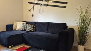 A dark blue sectional sofa with patterned cushions, a red and black rug, and a potted plant. - OTILIA apartment (Zell am See)