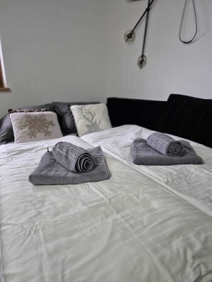 A neatly made bed with two rolled-up towels and a black headboard. - OTILIA apartment (Zell am See)