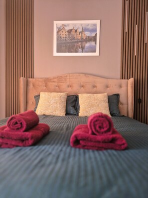 A neatly made bed with rolled towels, a headboard, and a framed picture of a cityscape on the wall. - OTILIA apartment (Zell am See)