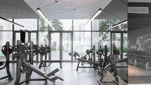 Une salle de sport moderne dotée de grandes fenêtres, de divers équipements d’entraînement en musculation et offrant une vue sur la ville.