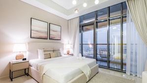 Une chambre à coucher moderne avec un grand lit, des lampes de chevet, une table de nuit et une vue sur la ville grâce à de grandes fenêtres.