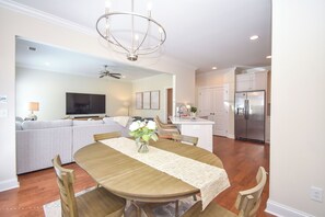 A modern kitchen with a built-in refrigerator, a dining area with a wooden table and chairs, and a living room with a sofa and television.