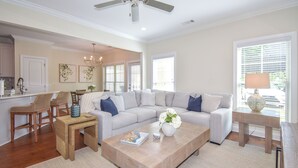 A spacious living room with a grey sectional sofa, a wooden coffee table, wicker chairs, and a kitchen area in the background. - Southern Charmer in Auburn, condo sleeps 8! Comes w/gameday parking pass! (Auburn)