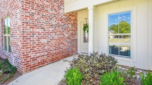 A brick building with a white door and window, a small garden with plants, and a clear sky. - Southern Charmer in Auburn, condo sleeps 8! Comes w/gameday parking pass! (Auburn)
