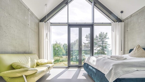 Et moderne soveværelse med en stor skydedør til en balkon, en grøn sofa og en seng med lyseblå sengegavl.