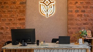 A reception desk with two computer monitors, a decorative logo, and an air conditioning unit on the wall. - Yashvrinda Hotel and Resort (Jodhpur)