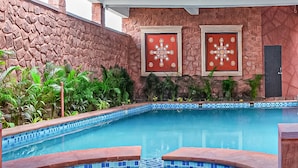 A swimming pool with a stone wall and tiled edge, surrounded by greenery. - Yashvrinda Hotel and Resort (Jodhpur)