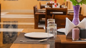 A dining table set with plates, cutlery, and a vase of flowers. - Yashvrinda Hotel and Resort (Jodhpur)