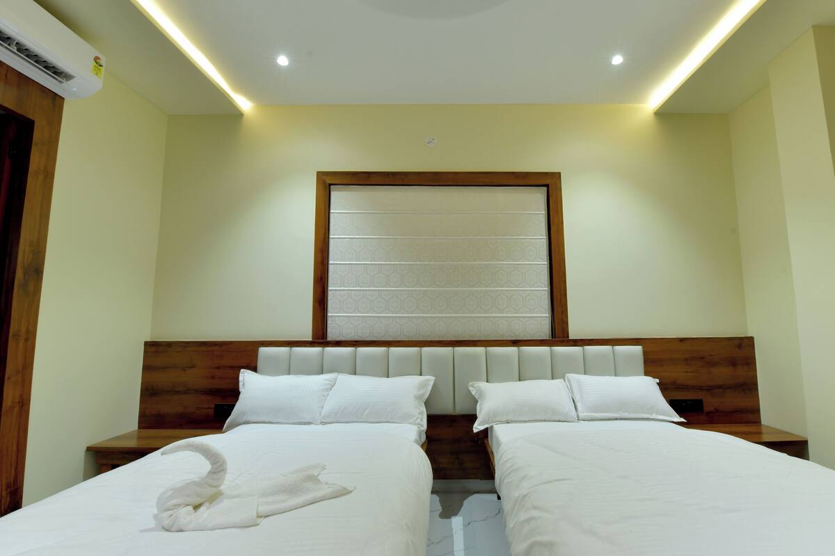 Une chambre d’hôtel avec deux lits, une tête de lit en bois, une grande fenêtre ornée d’un motif géométrique et une serviette sur le lit.