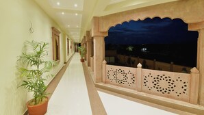 A corridor with a tiled floor, potted plants, and a decorative railing with geometric patterns. - Yashvrinda Hotel and Resort (Jodhpur)