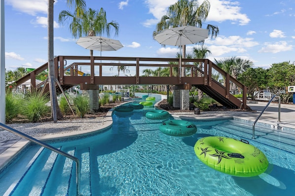A swimming pool with clear blue water, surrounded by palm trees and a wooden bridge.
