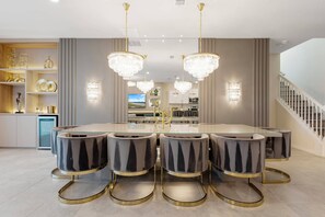 Un comedor moderno con una mesa de vidrio, cuatro sillas tapizadas y dos candelabros.