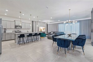 Una cocina moderna con una isla central, taburetes de bar y una zona de comedor con una mesa grande y sillas.