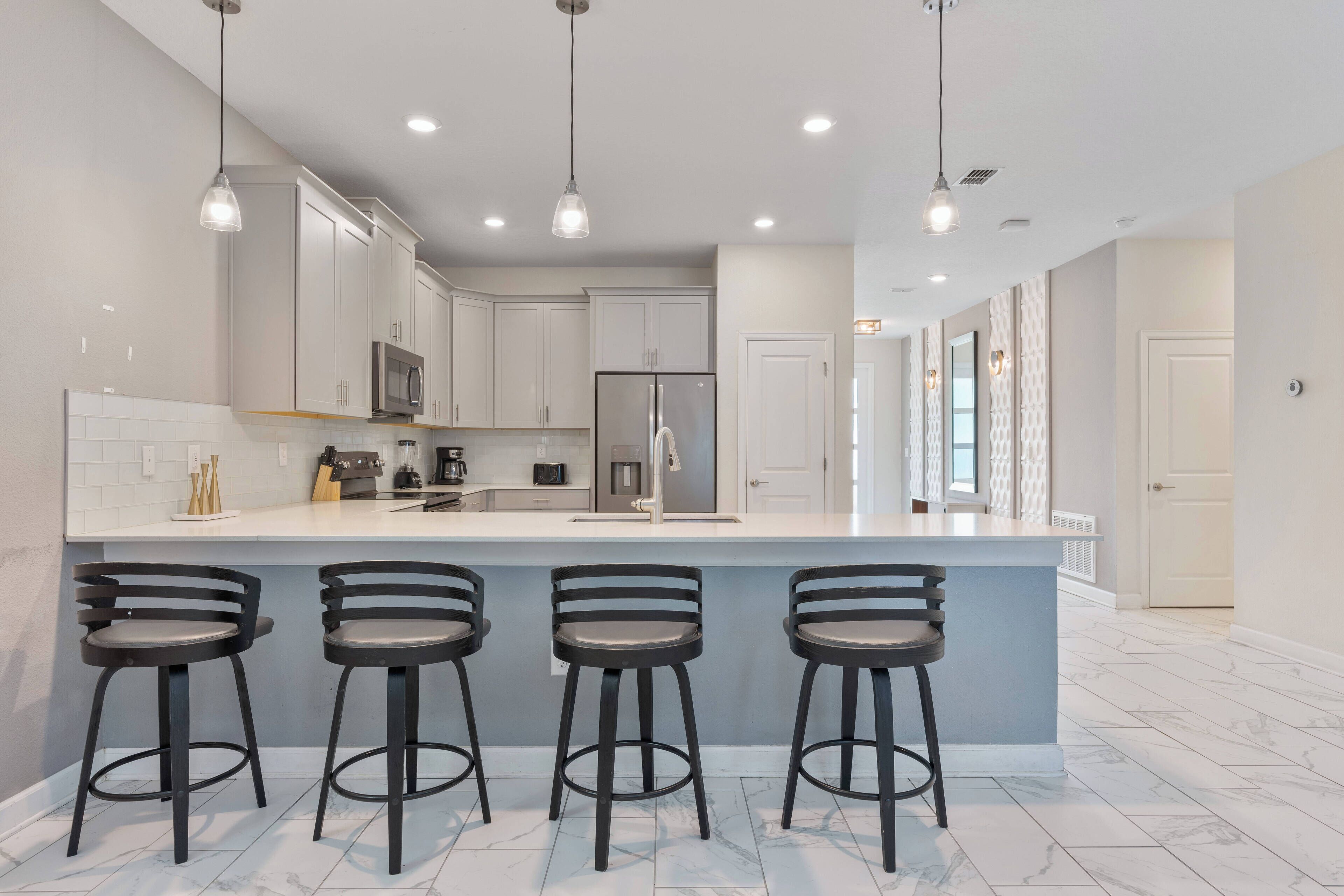 A modern kitchen with a central island, bar stools, stainless steel appliances, and pendant lighting.