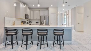A modern kitchen with a central island, bar stools, stainless steel appliances, and pendant lighting. - 9BR house with private pool in Champions Gate (Kissimmee)