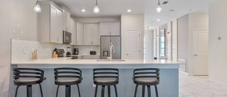 A modern kitchen with a central island, bar stools, stainless steel appliances, and pendant lighting.