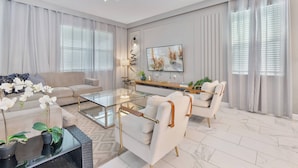 A modern living room with a glass coffee table, white sofas, and a large window with sheer curtains. - 9BR house with private pool in Champions Gate (Kissimmee)