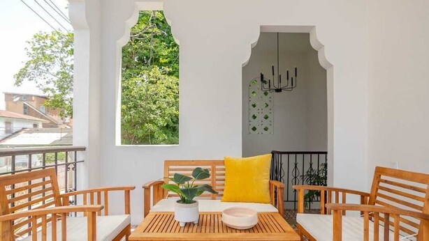 Un balcón con una mesa y sillas de madera, una planta en maceta y una almohada amarilla.
