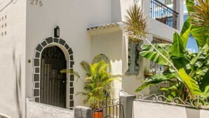 Un edificio blanco con una puerta numerada, un acceso con rejas y plantas en macetas.